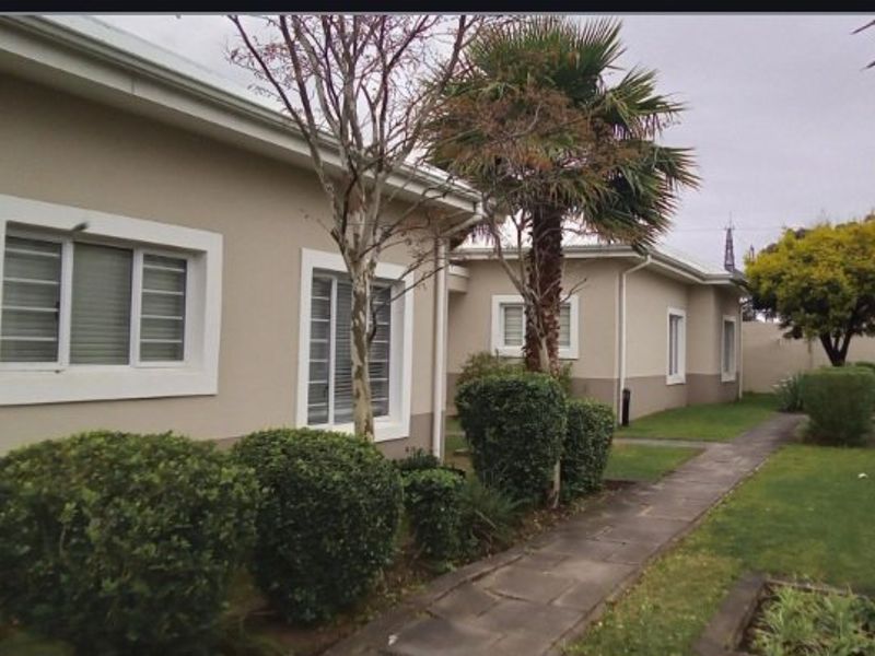 A view of the rear exterior of the townhouse, featuring a paved walkway, established garden, and security bars on the windows.