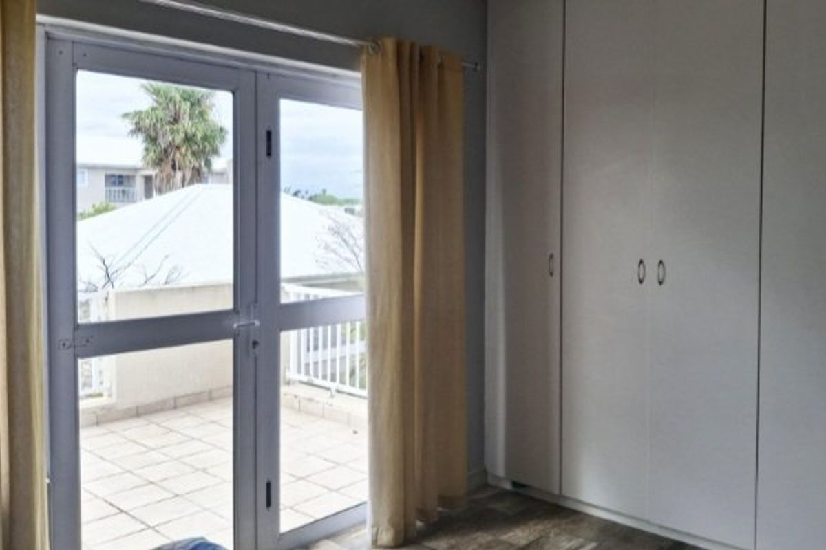Bedroom featuring built-in cupboards and direct access to a private tiled balcony through double glass doors.