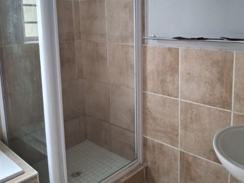 A functional bathroom featuring a glass-enclosed shower, neutral wall tiling, and a pedestal basin, offering a clean and practical layout.