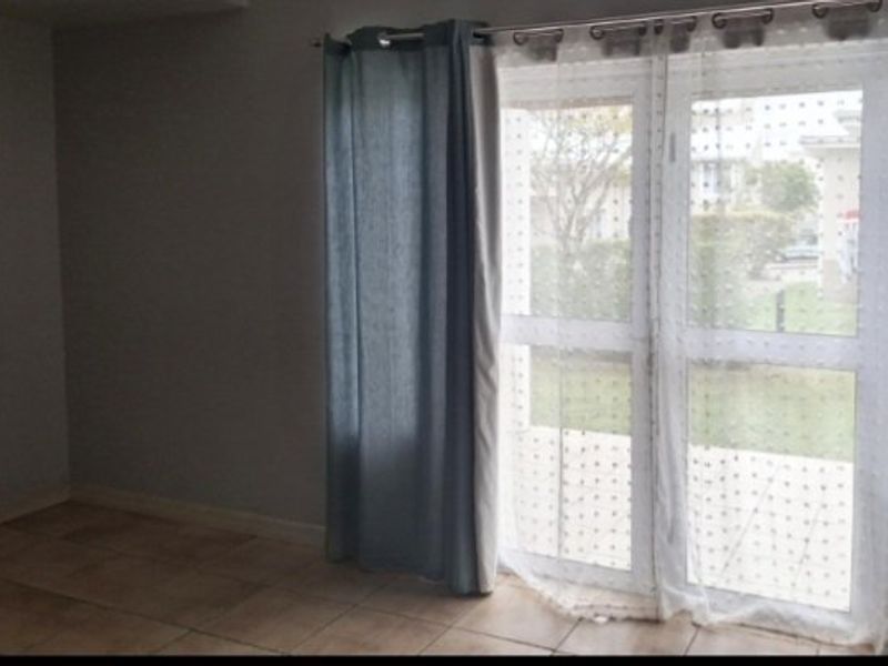 An empty living room featuring tiled flooring and a glass sliding door providing access to the exterior.