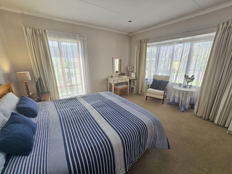 A well-lit bedroom featuring carpeted flooring, a large bay window with curtains, and recessed ceiling lighting, offering a comfortable and functional living space.