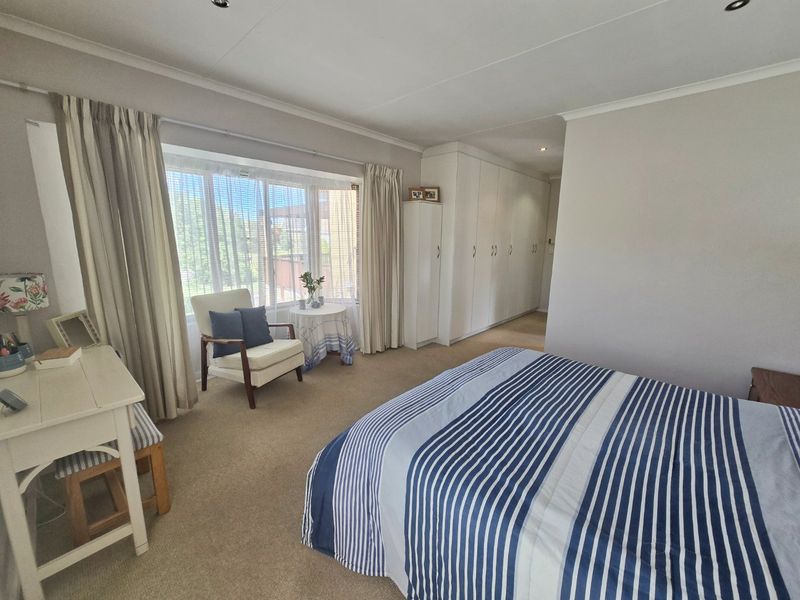 Spacious bedroom featuring extensive built-in cupboards, a large bay window providing natural light, and neutral carpeted flooring.