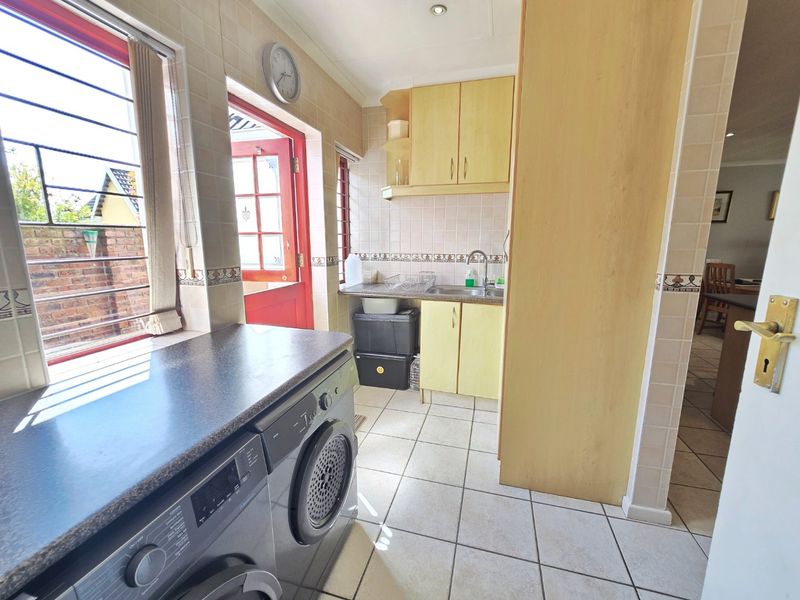 Functional scullery area featuring tiled flooring, built-in cabinetry, stainless steel sink, and direct access to the exterior.
