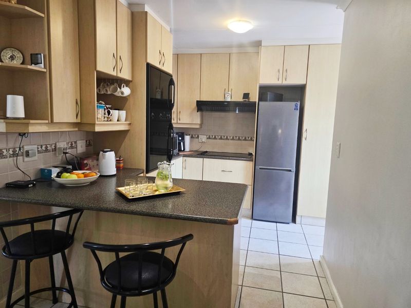 A functional kitchen featuring light wood cabinetry, dark laminate countertops, tiled flooring, and integrated appliances including an oven and extractor fan.