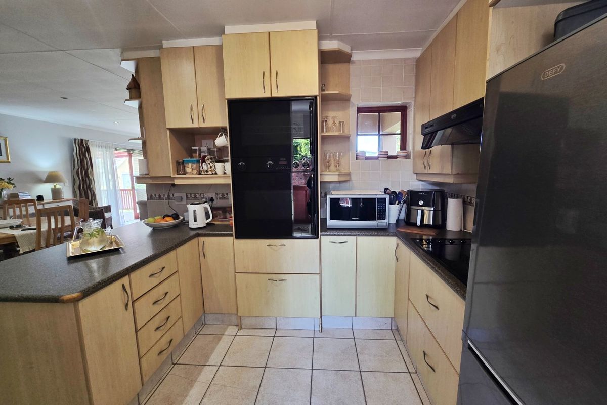 A functional U-shaped kitchen featuring light wood cabinetry, dark laminate countertops, built-in oven, extractor fan, and tiled flooring, with an open-plan layout.