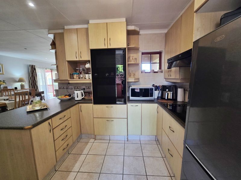 A functional U-shaped kitchen featuring light wood cabinetry, dark laminate countertops, built-in oven, extractor fan, and tiled flooring, with an open-plan layout.
