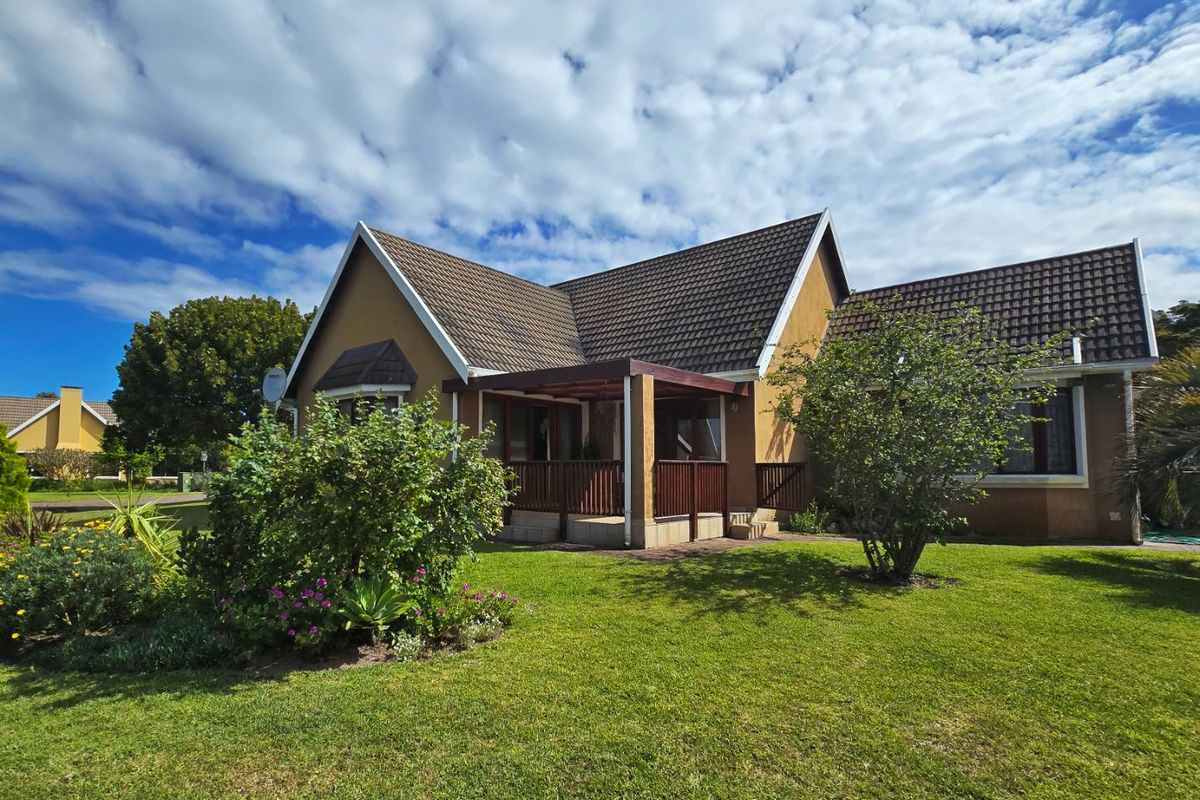 A well-maintained rear exterior view of the house featuring a covered patio with timber balustrades, set within a neat, landscaped garden.