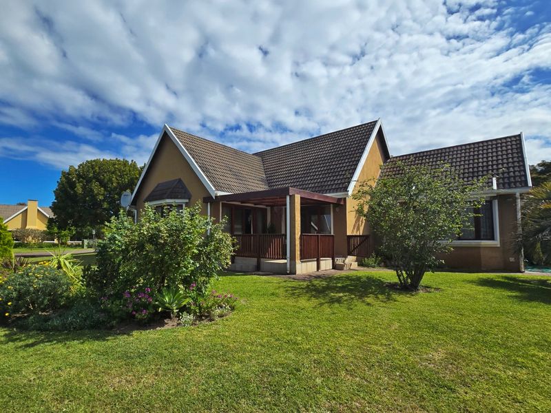 A well-maintained rear exterior view of the house featuring a covered patio with timber balustrades, set within a neat, landscaped garden.