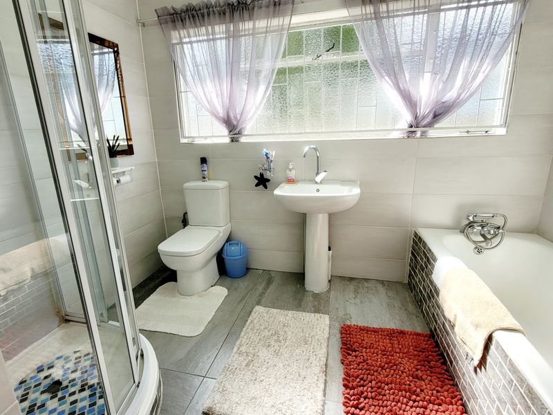 A functional bathroom featuring a pedestal basin, a separate shower enclosure, and a bathtub with tiled finishes throughout.