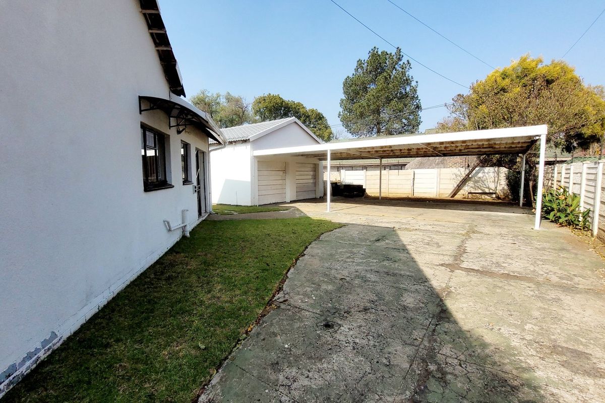 Rear exterior view featuring a concrete driveway, a covered carport, a detached garage structure, and a precast concrete boundary wall.