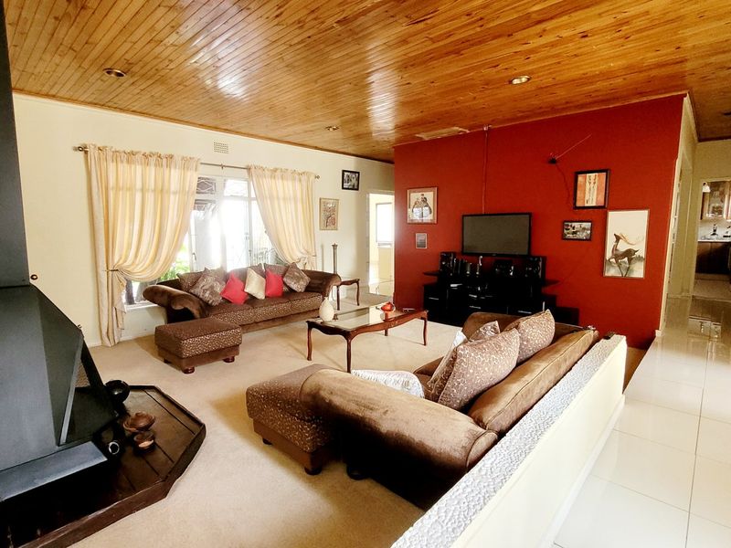 Spacious living room featuring a wood-paneled ceiling, a prominent freestanding fireplace, and a mix of tiled and carpeted flooring.