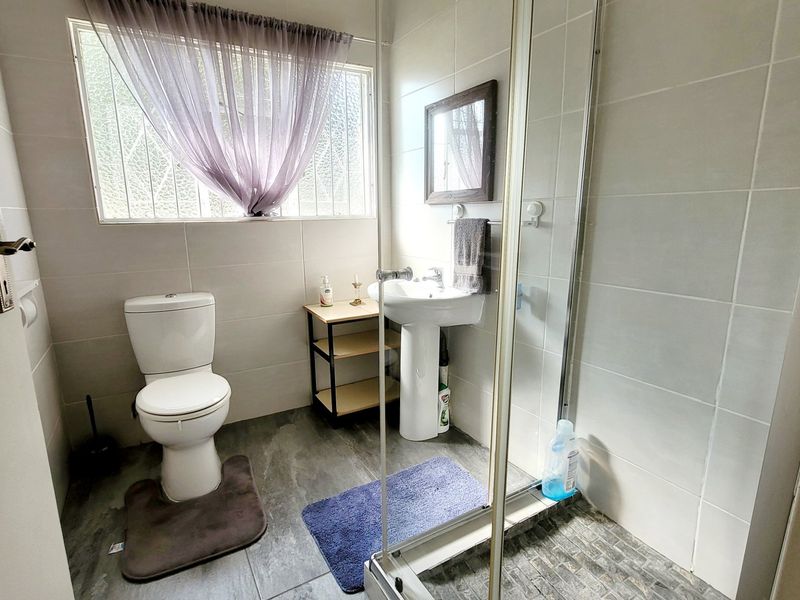 A functional bathroom featuring a pedestal basin, toilet, and a glass-enclosed shower with neutral wall and floor tiling.