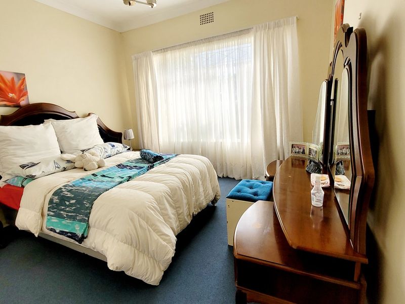 A well-lit bedroom featuring carpeted flooring, a large window with curtains, and a ceiling ventilation vent.