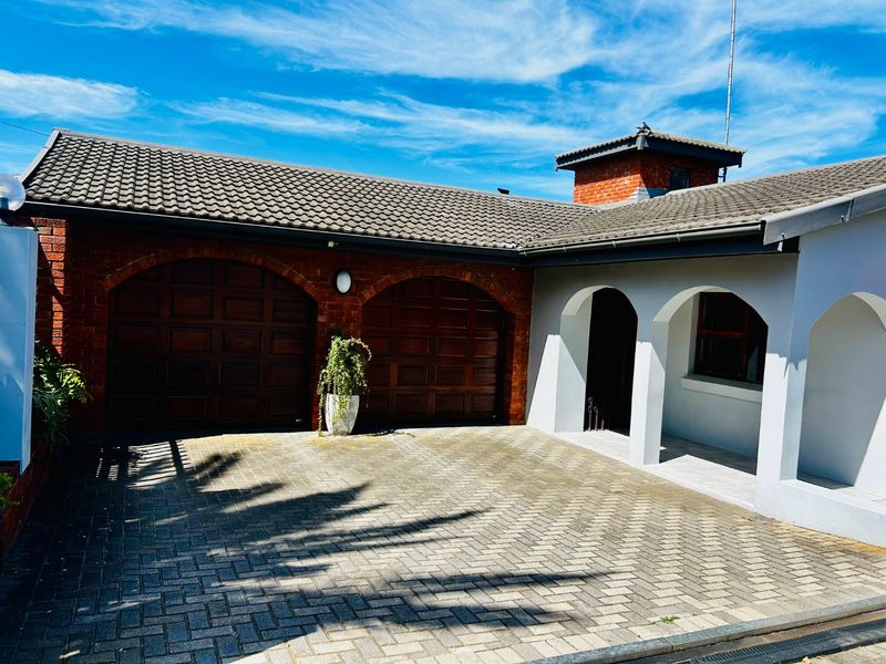 Front elevation of the property featuring a double garage with arched wooden doors, a paved driveway, and a covered entrance area.