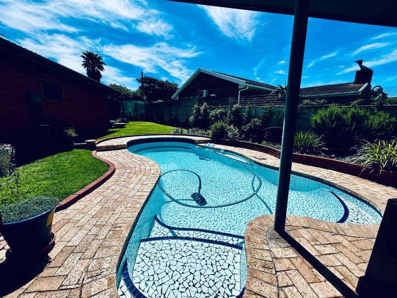 Outdoor pool area featuring a mosaic-tiled swimming pool, brick paving, and a covered patio space overlooking the garden.