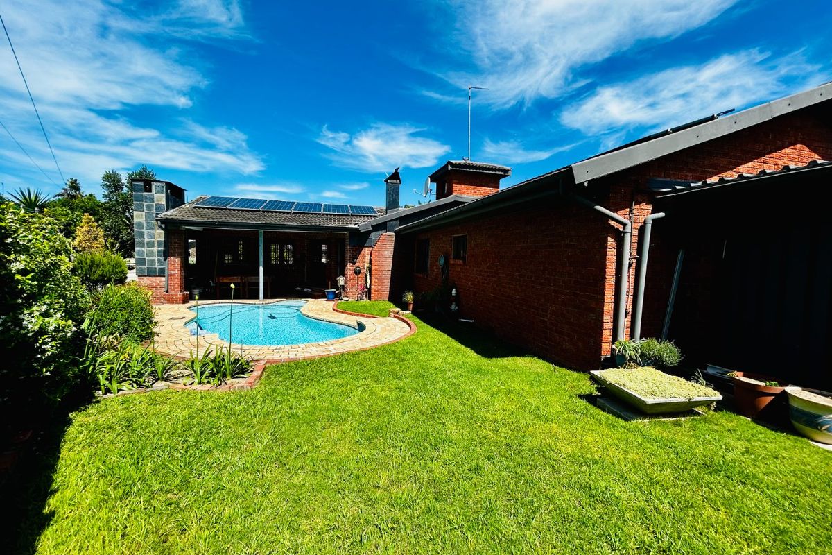 Rear exterior view featuring a brick house, a swimming pool with paved surround, a well-maintained lawn, and roof-mounted solar panels.