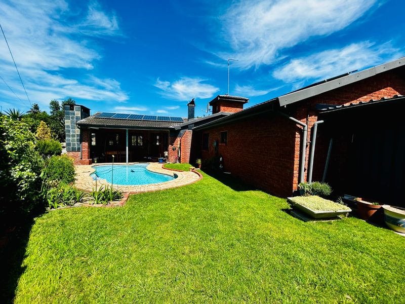 Rear exterior view featuring a brick house, a swimming pool with paved surround, a well-maintained lawn, and roof-mounted solar panels.