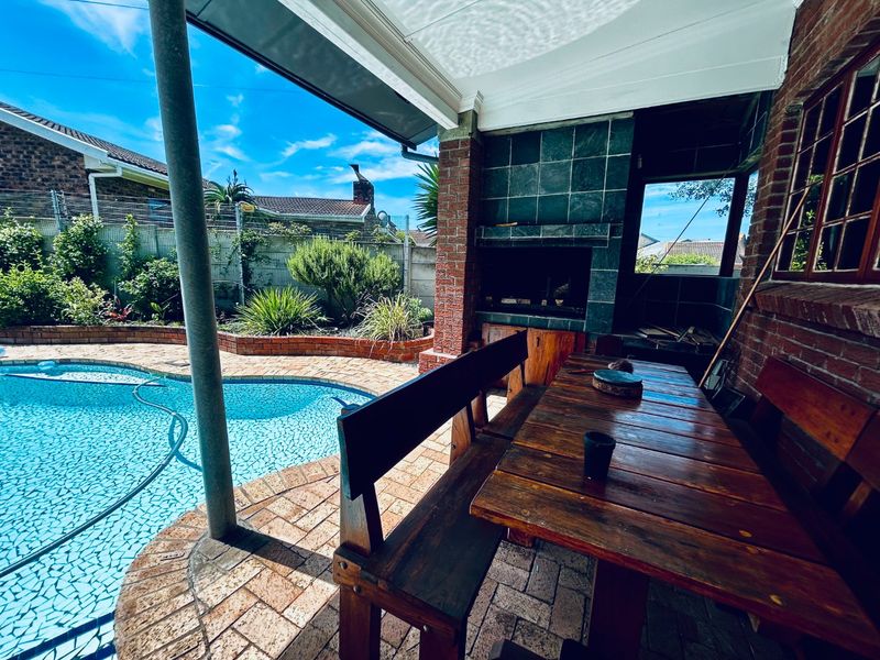 Outdoor entertainment area featuring a covered patio with a built-in braai, overlooking a swimming pool with brick paved surrounds.