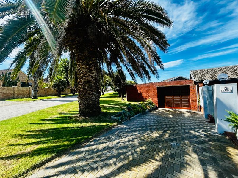 Front exterior view of the property featuring a paved driveway, brick boundary wall, garage access, and a large mature palm tree.