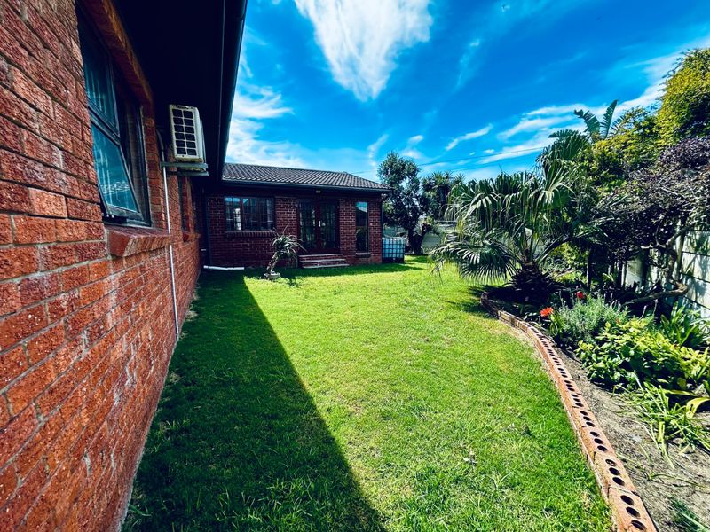 A well-maintained rear garden featuring a classic red brick facade, established landscaping, and a neat lawn area.