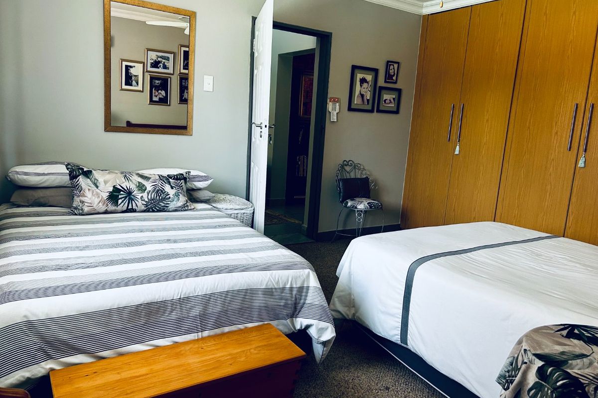 A spacious bedroom featuring built-in wooden cupboards, carpeted flooring, and a ceiling fan, offering a functional layout with direct access to an adjoining room.