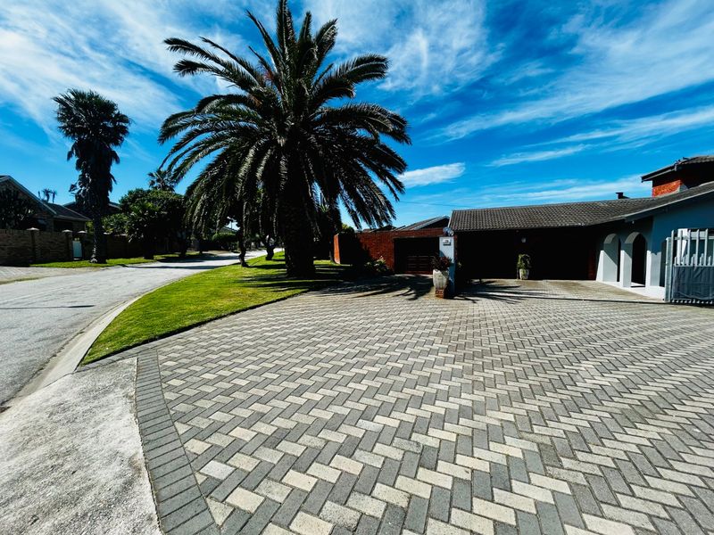 A well-maintained front exterior view featuring a spacious paved driveway, established palm tree, and access to the garage.