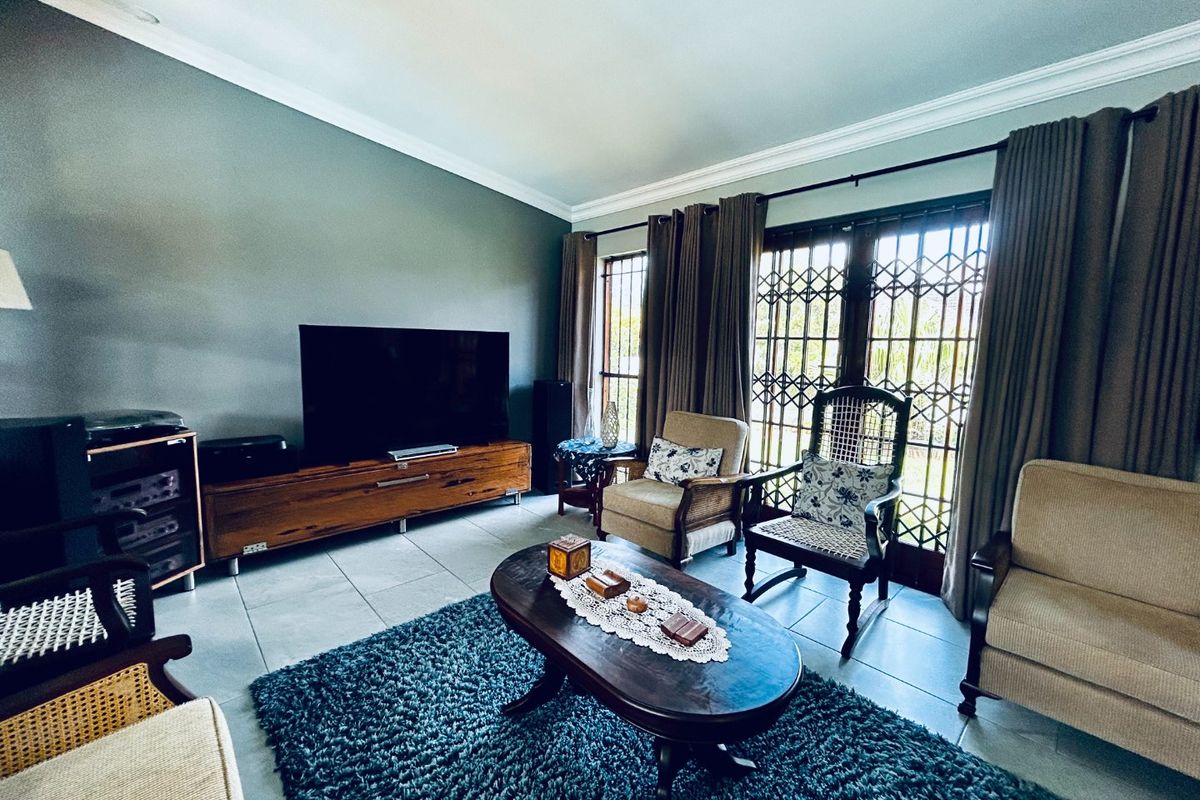 A comfortable living room featuring tiled flooring, crown molding, and large sliding glass doors with security gates providing access to the outdoors.
