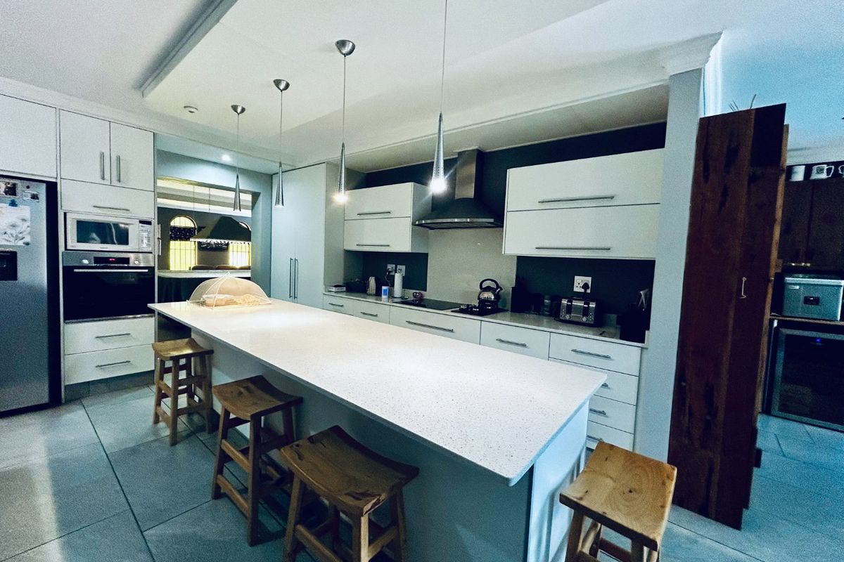 Modern kitchen featuring a large central island with stone countertop, sleek white cabinetry, built-in appliances, and contemporary pendant lighting.