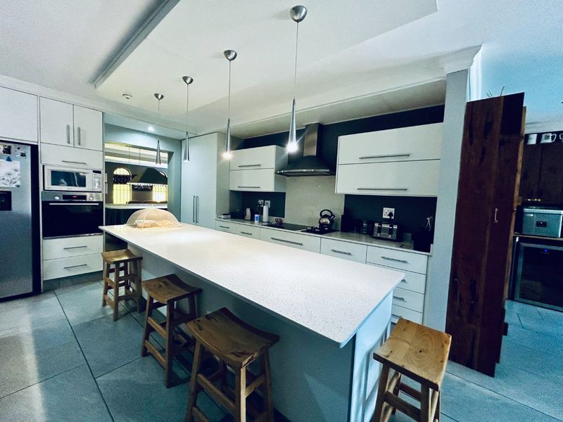 Modern kitchen featuring a large central island with stone countertop, sleek white cabinetry, built-in appliances, and contemporary pendant lighting.