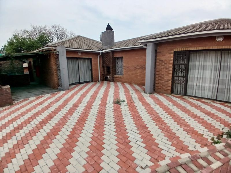 Rear exterior view featuring a large patterned brick paved patio area, built-in braai, and multiple sliding door access points to the home.