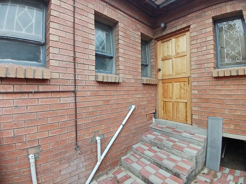 Rear exterior view showing a brick facade, timber stable door, and tiled steps with visible external plumbing and security window bars.