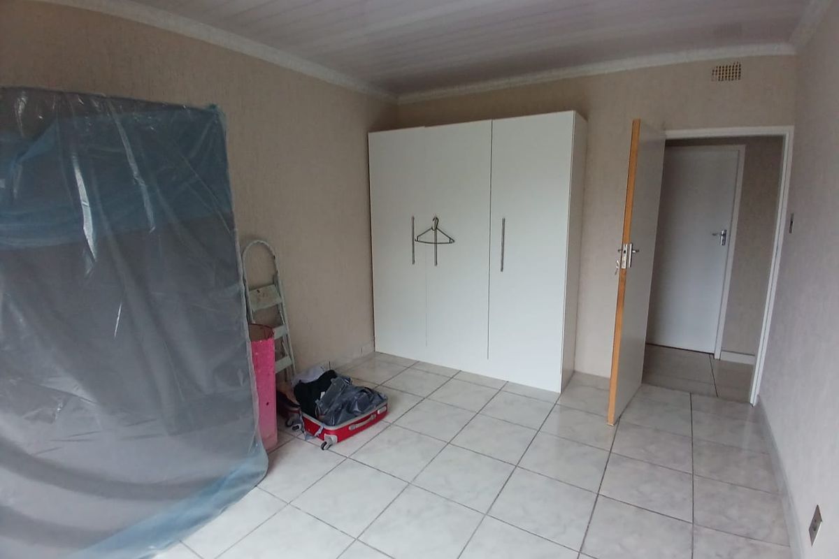 A simple bedroom featuring tiled flooring, a built-in wardrobe, and ceiling cladding, offering a clean and functional space.