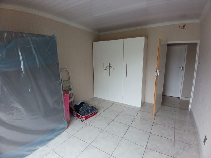 A simple bedroom featuring tiled flooring, a built-in wardrobe, and ceiling cladding, offering a clean and functional space.