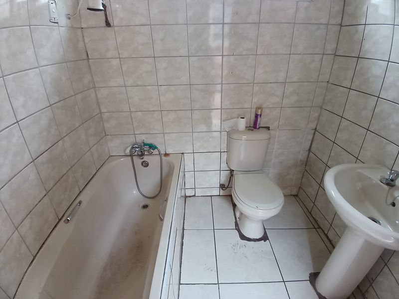 A functional bathroom featuring a bathtub, pedestal basin, and toilet with full-height wall tiling and tiled flooring.