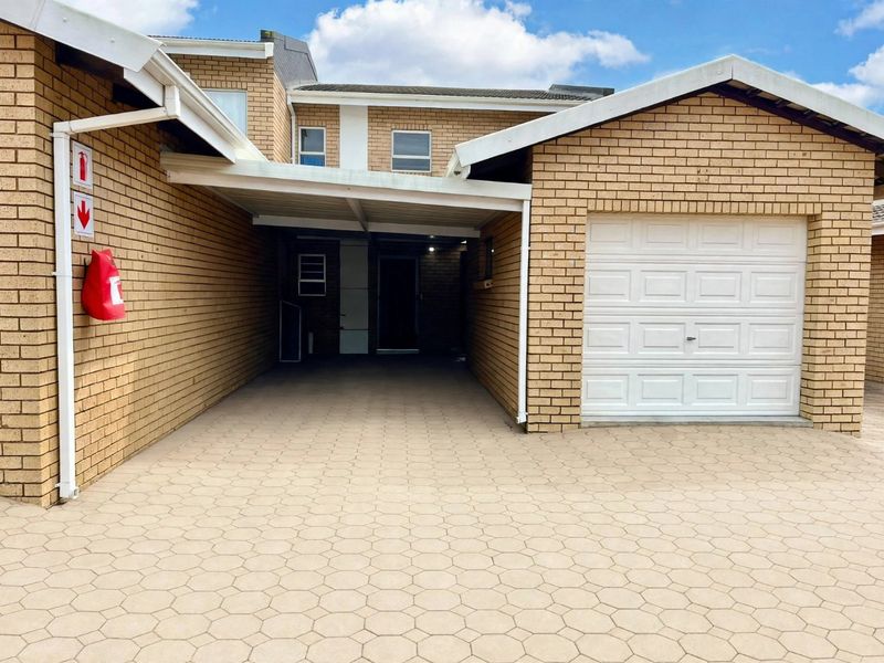 Front exterior view of the apartment featuring a brick facade, a single garage, and a covered carport area with paved driveway.