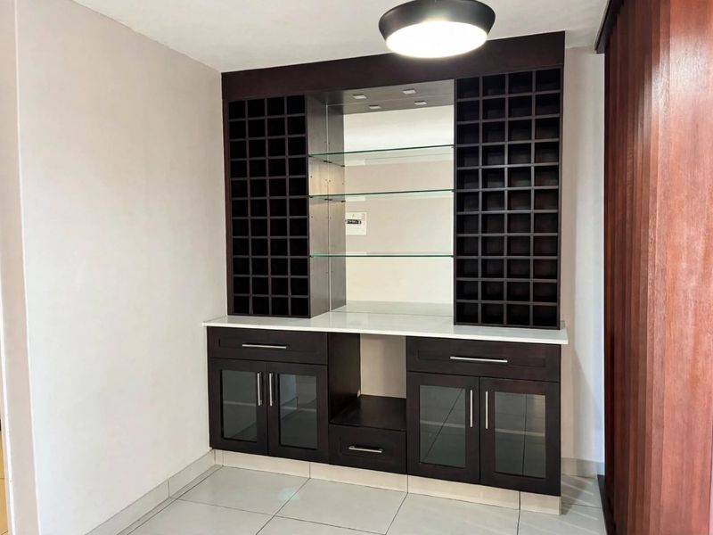 A modern built-in bar unit featuring dark wood cabinetry, glass shelving, a mirrored backsplash, and a stone countertop.