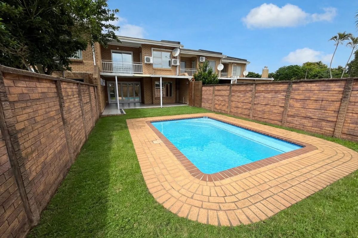 Rear view of the apartment featuring a private swimming pool, paved surround, lawn, and a covered patio area with an upper-level balcony.