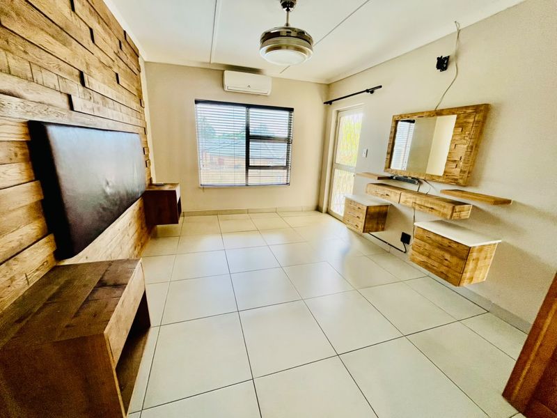 A spacious bedroom featuring tiled floors, a wall-mounted wooden headboard, floating vanity unit, and air conditioning, offering a clean and modern aesthetic.