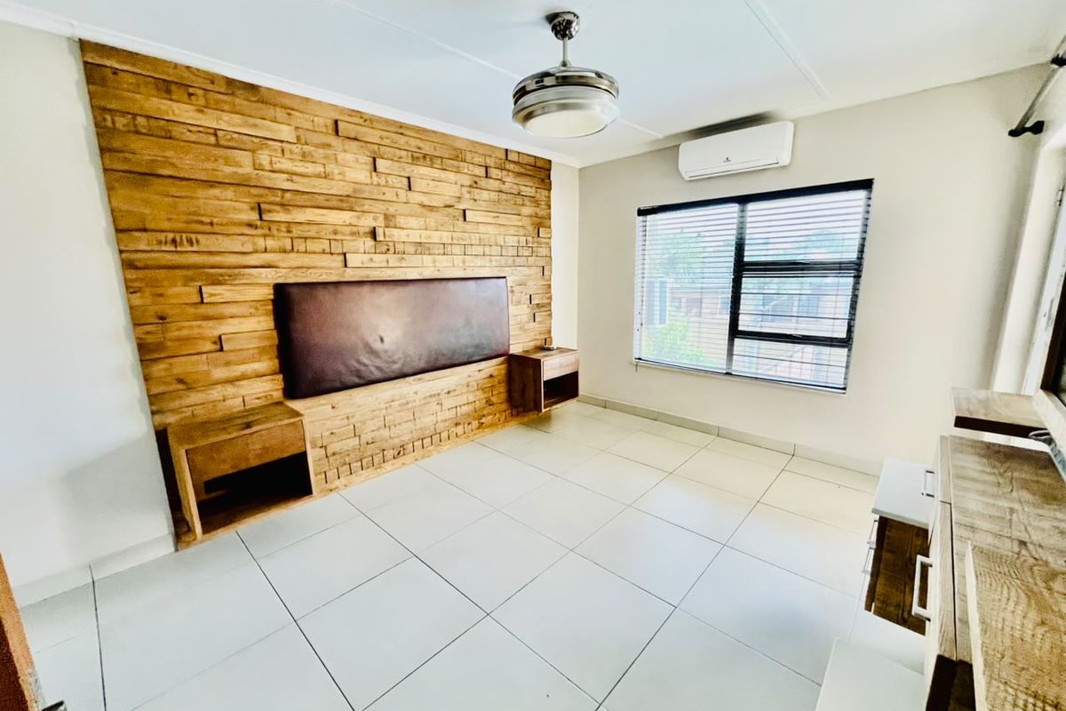 Spacious bedroom featuring a decorative timber feature wall with integrated headboard and bedside tables, tiled flooring, ceiling fan, and air conditioning unit.