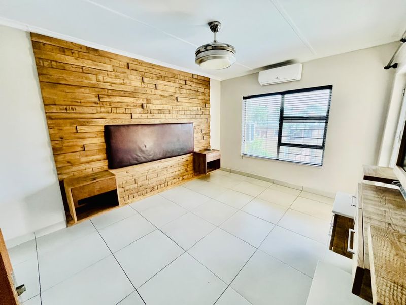 Spacious bedroom featuring a decorative timber feature wall with integrated headboard and bedside tables, tiled flooring, ceiling fan, and air conditioning unit.