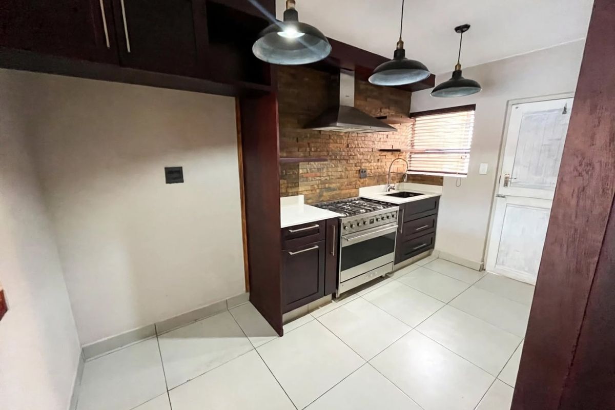 A functional kitchen featuring dark cabinetry, a stainless steel gas stove, exposed brick backsplash, and tiled flooring.