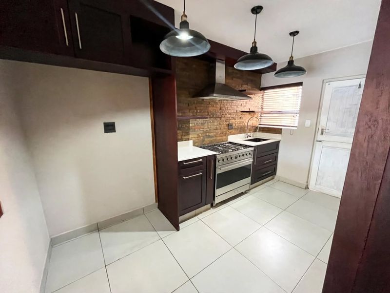 A functional kitchen featuring dark cabinetry, a stainless steel gas stove, exposed brick backsplash, and tiled flooring.