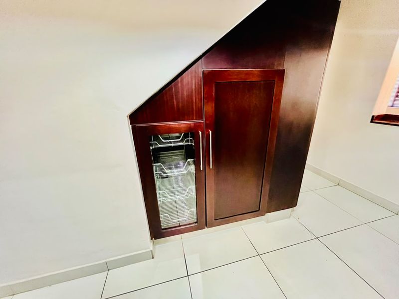 A functional under-stair storage area featuring custom dark wood cabinetry with integrated pull-out wire shelving and clean tiled flooring.