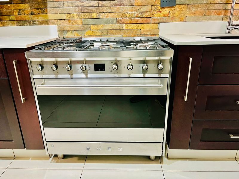 Modern kitchen featuring a high-end stainless steel Smeg gas stove, dark wood cabinetry, quartz countertops, and a decorative stone veneer backsplash.