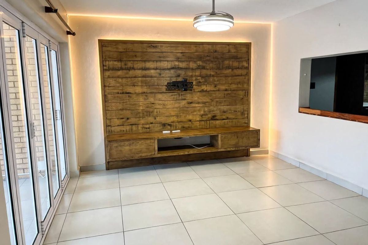 A bright, modern living area featuring a custom built-in wooden media console, ambient LED lighting, tiled floors, and large sliding doors leading outdoors.