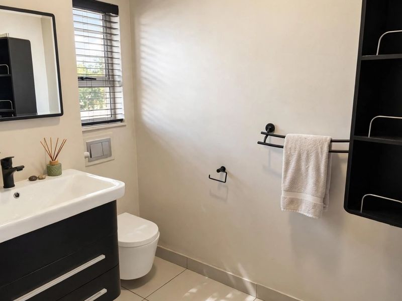 A modern bathroom featuring a wall-mounted vanity, basin, wall-hung toilet, and sleek black fixtures, complemented by neutral floor tiles and natural light.