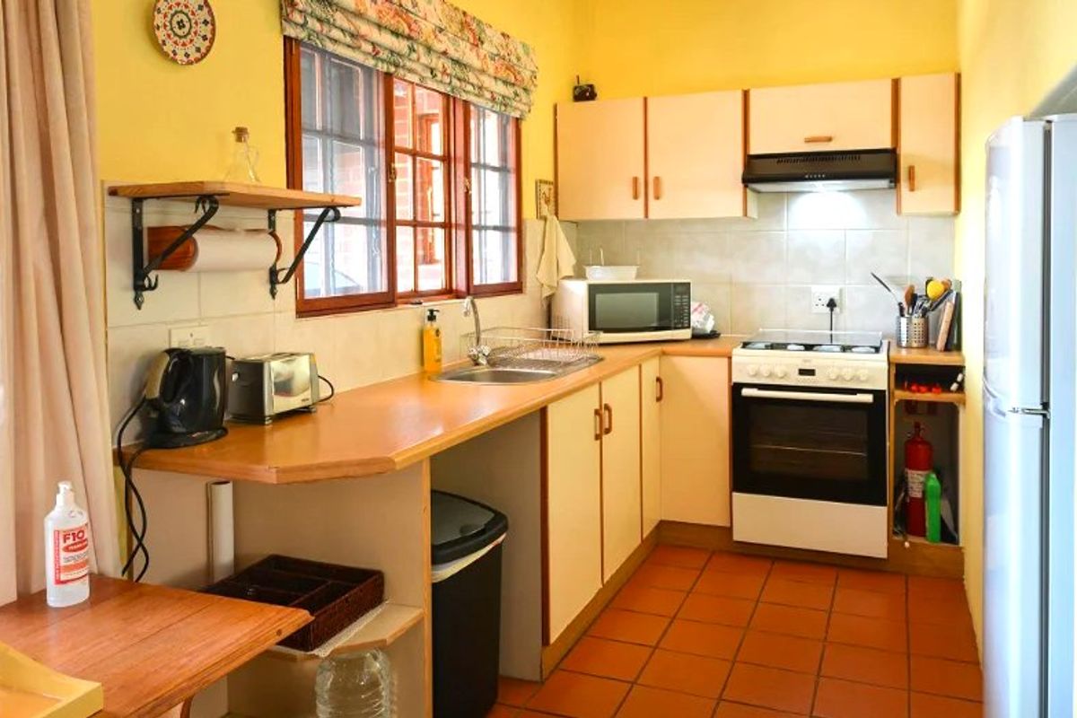 A functional kitchen featuring laminate countertops, built-in cabinetry, a tiled backsplash, and a freestanding oven with an extractor fan.