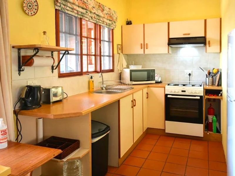 A functional kitchen featuring laminate countertops, built-in cabinetry, a tiled backsplash, and a freestanding oven with an extractor fan.