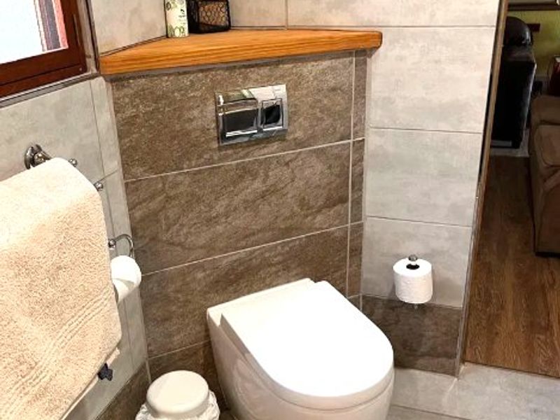 A modern bathroom featuring a wall-mounted toilet with a dual flush system, complemented by neutral-toned wall and floor tiling and a built-in corner shelf.