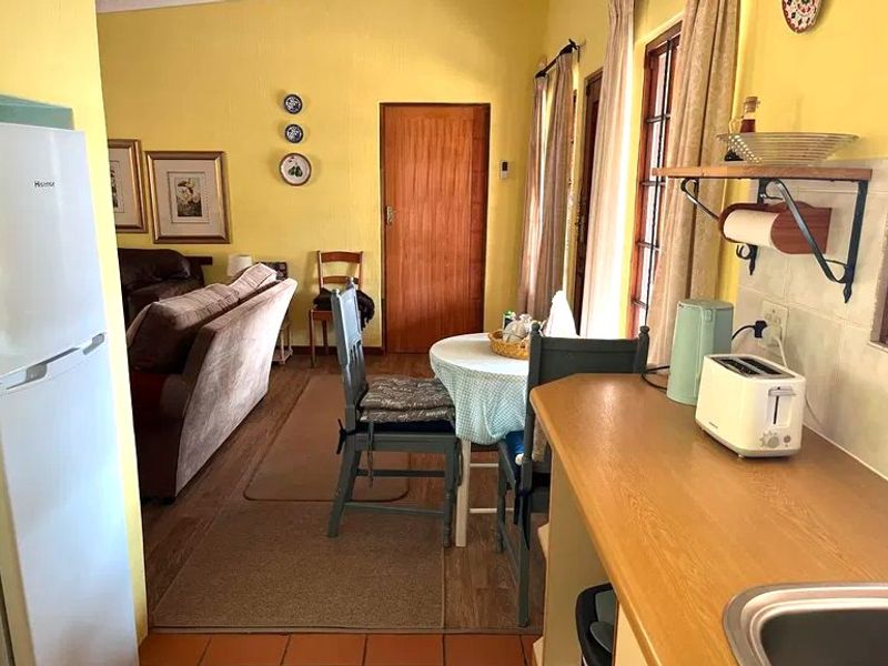 Open-plan living and kitchen area featuring a mix of tiled and laminate flooring, wooden door, and functional kitchen workspace with wall-mounted shelving.